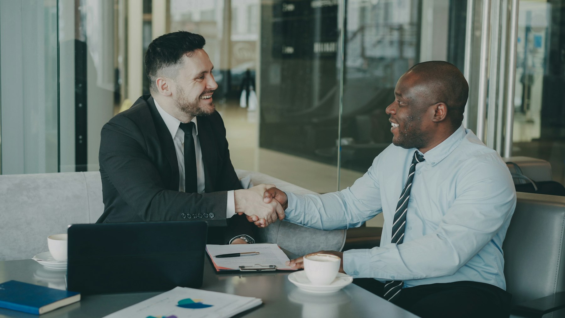 Two business advisers shaking hands across a meeting table